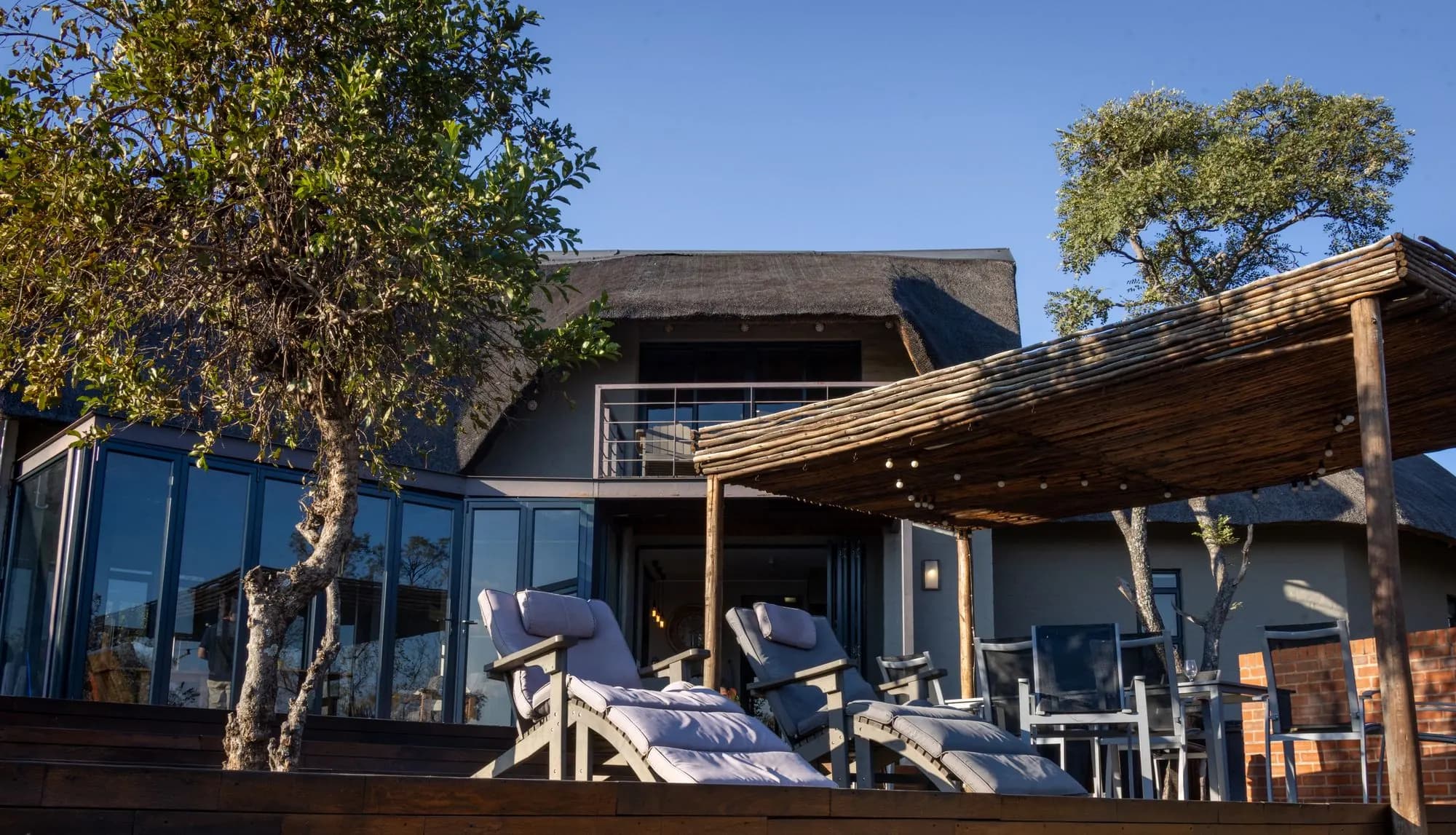 A thatched bush house with a covered patio and loungers